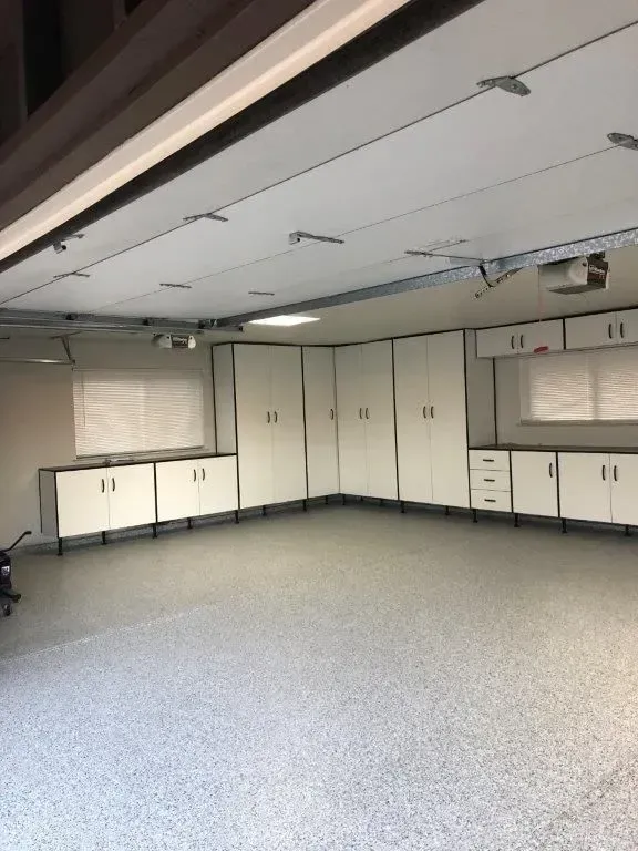Garage with white cabinets, dark countertops, and speckled floor.  Garage door open.