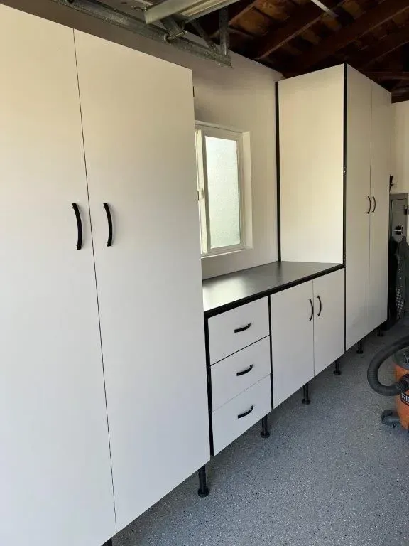 White garage storage cabinets with black accents and handles; a window is centered.
