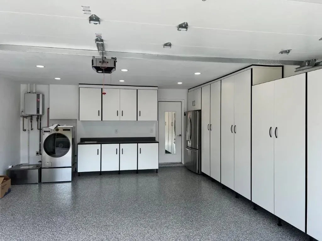 White-walled garage with gray epoxy floor, storage cabinets, appliances (washer/dryer, refrigerator), and a garage door opener.