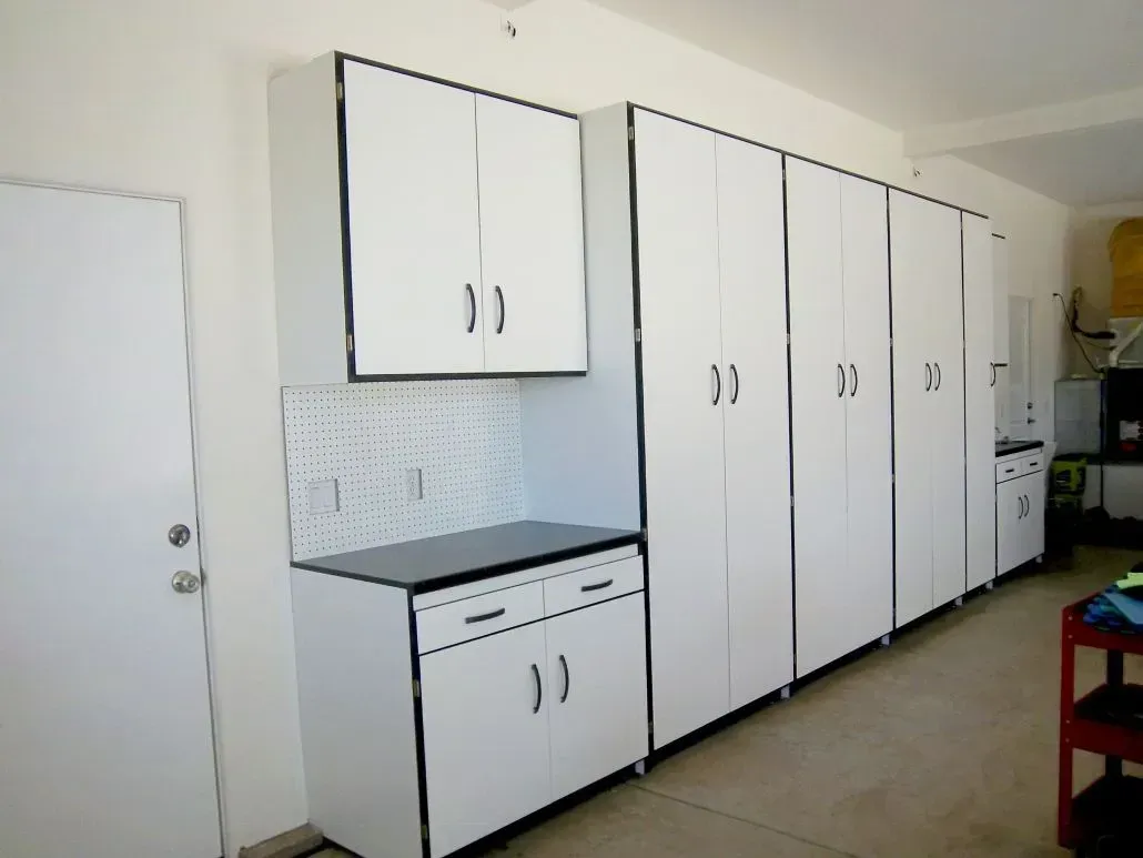 White garage storage cabinets against a white wall; includes cabinets, drawers, and a pegboard.