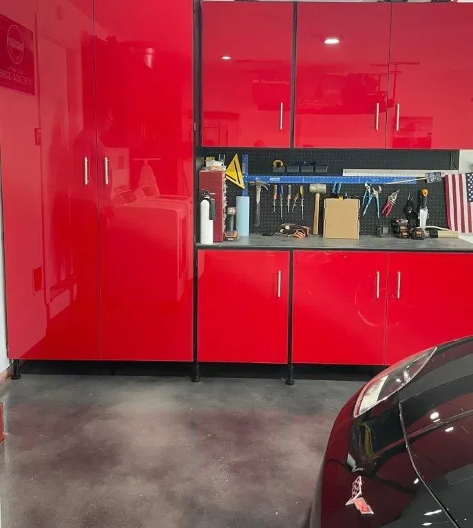 Red cabinets and workbench in a garage. A car is parked in the foreground.