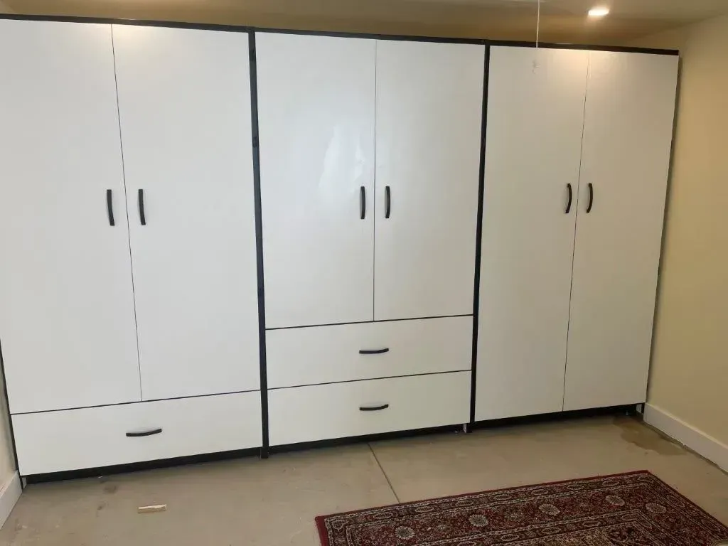 Three white storage cabinets with black trim and handles, in a room with a rug on the floor.