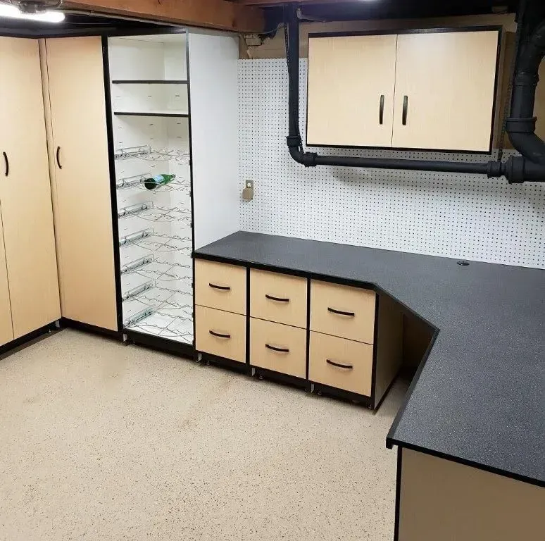 Garage workshop with beige cabinets, black countertops, and a pegboard wall.