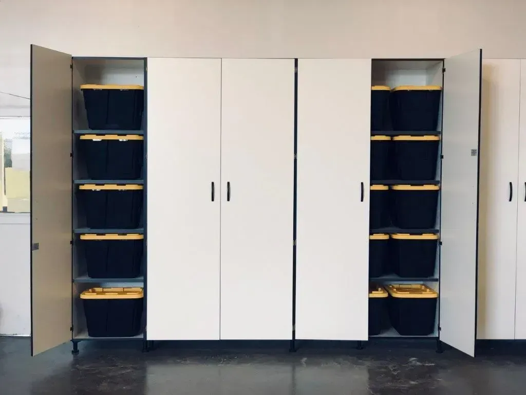 White storage cabinets with black and yellow bins inside, in a garage setting.