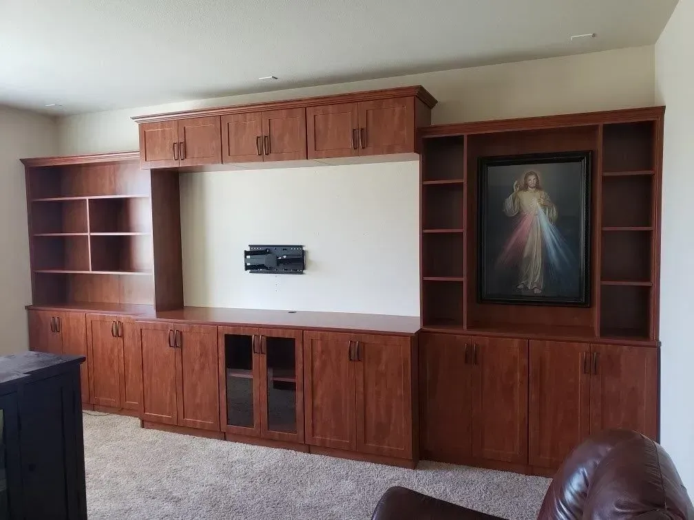 Custom wood built-in cabinet with upper and lower cabinets and shelves, framed religious artwork.