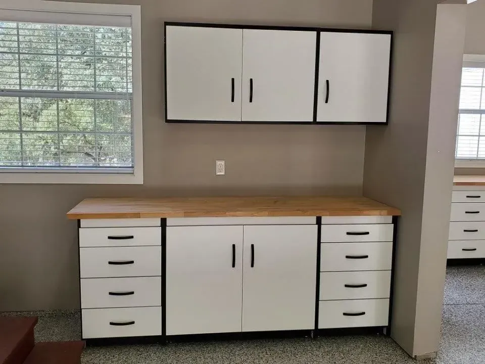 White and black cabinets with wooden countertop in a garage setting.