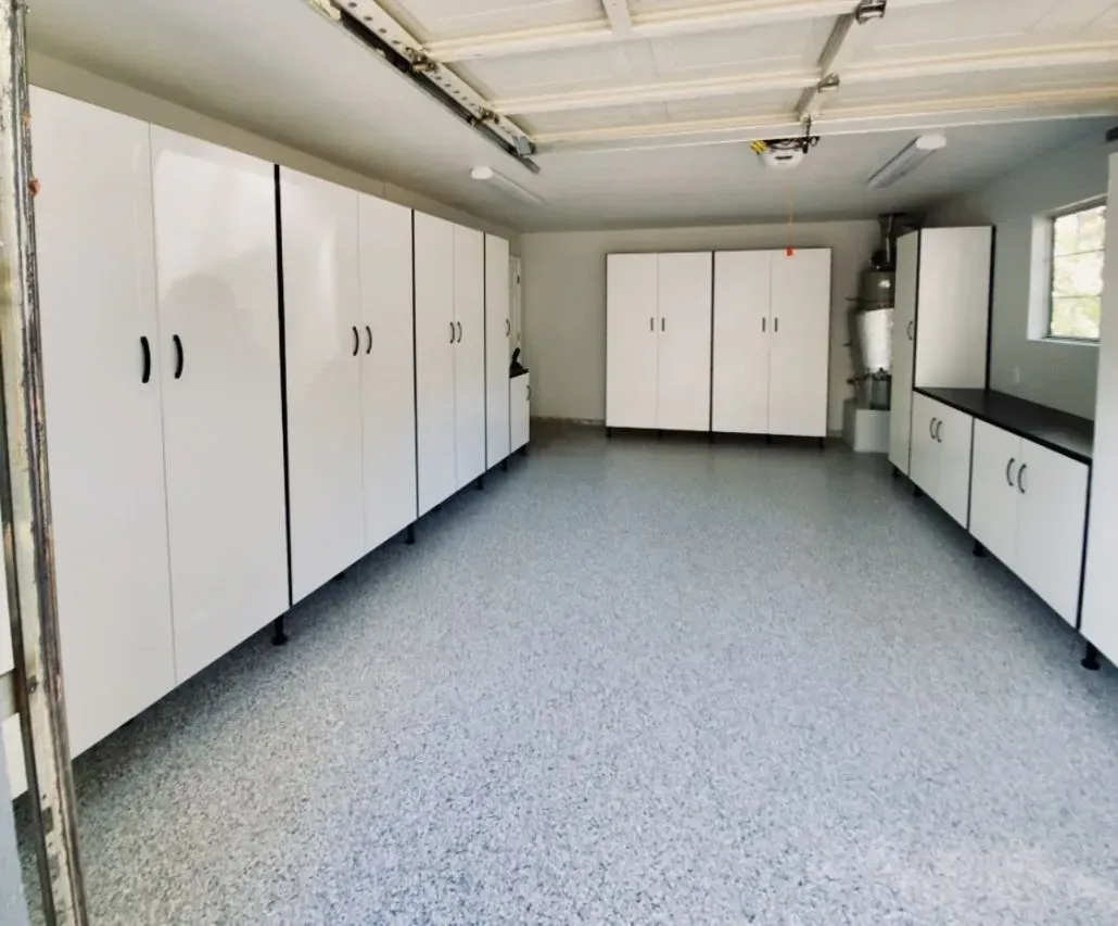 White-walled garage with numerous white storage cabinets and a speckled gray floor.
