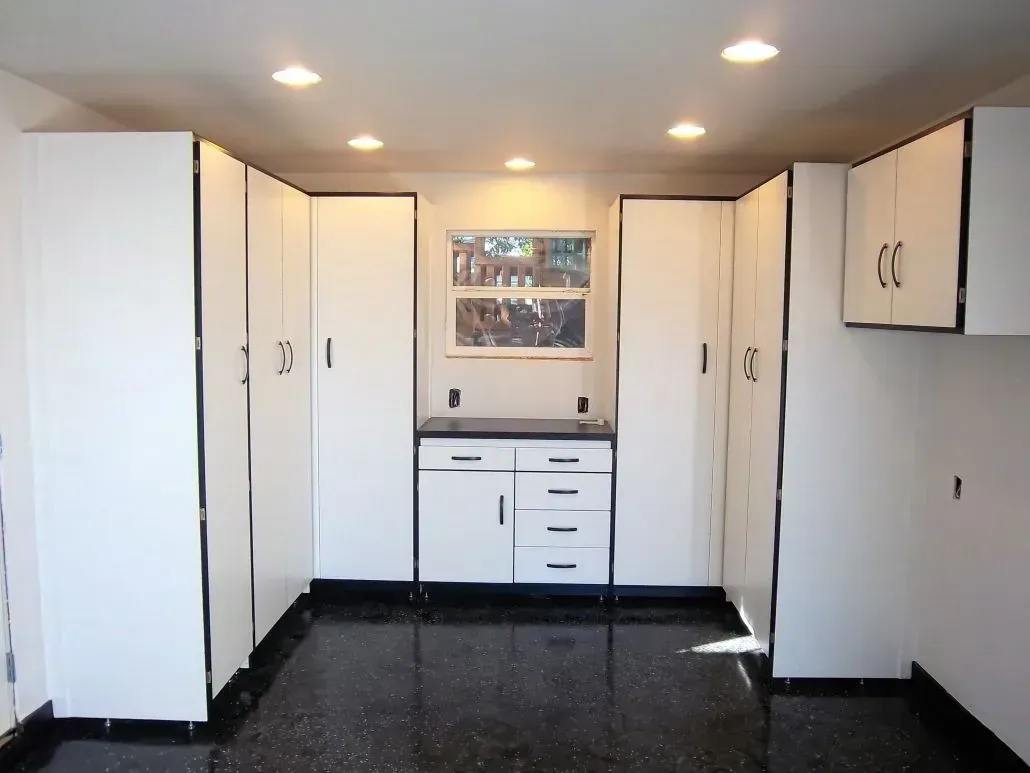 White cabinets with black trim in a room with a black floor and a small window.