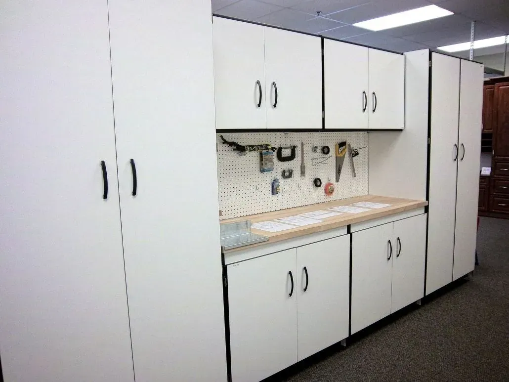 White storage cabinets and pegboard workbench in a garage setting.
