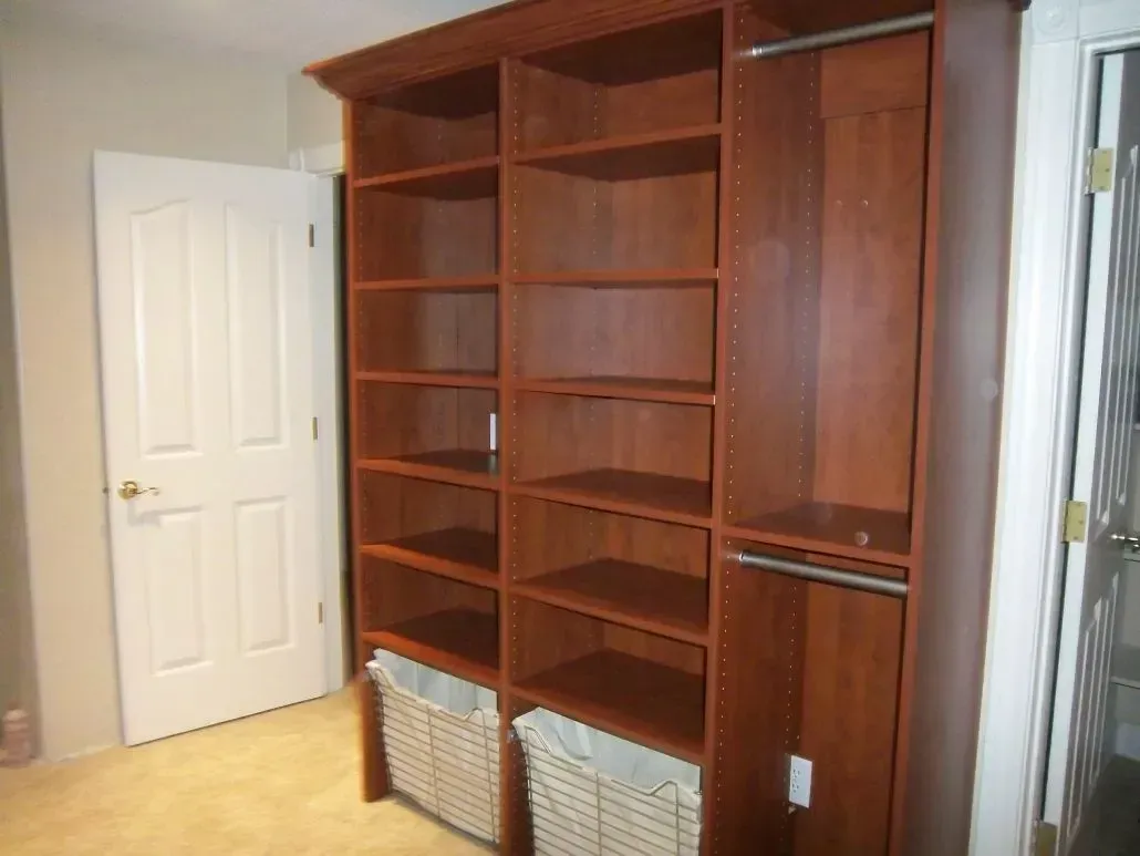 Built-in wooden closet with shelves and a hanging rod, next to a white door. Baskets are at the bottom.