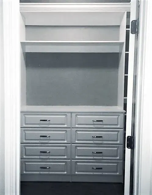 Built-in closet with drawers and shelves. White painted wood, chrome hardware, blue-gray wall.