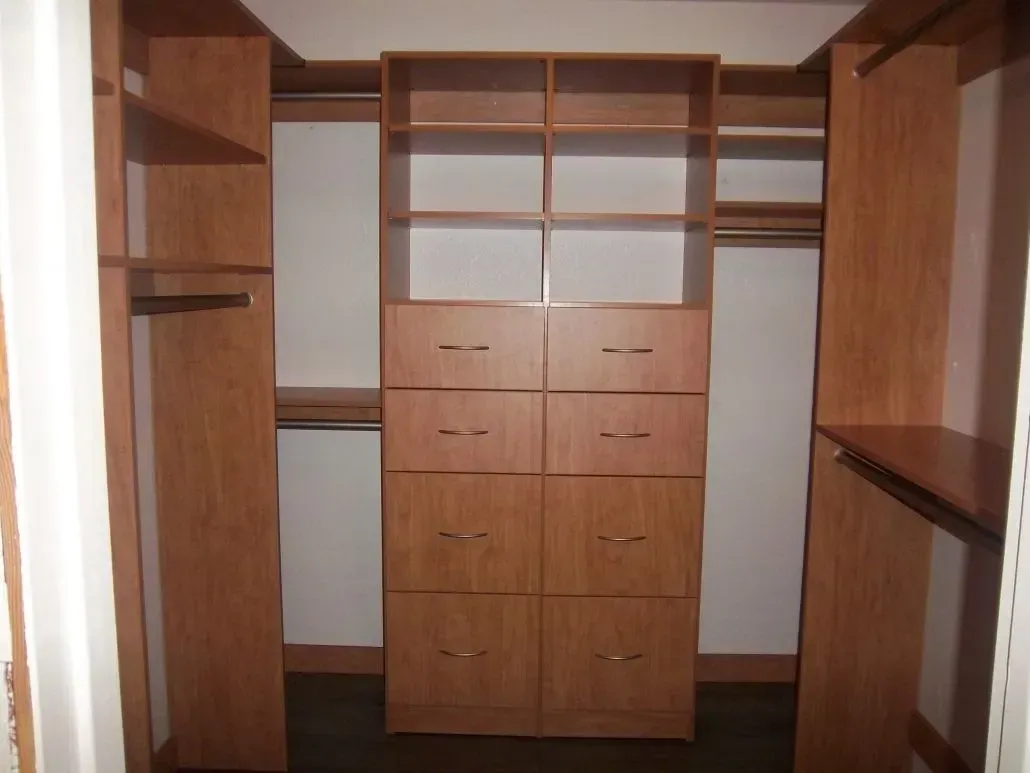 Wooden walk-in closet with shelves, drawers, and hanging rods.