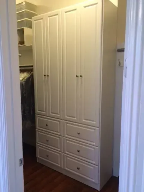 White built-in closet unit with six drawers and four doors in a doorway, wood floor.