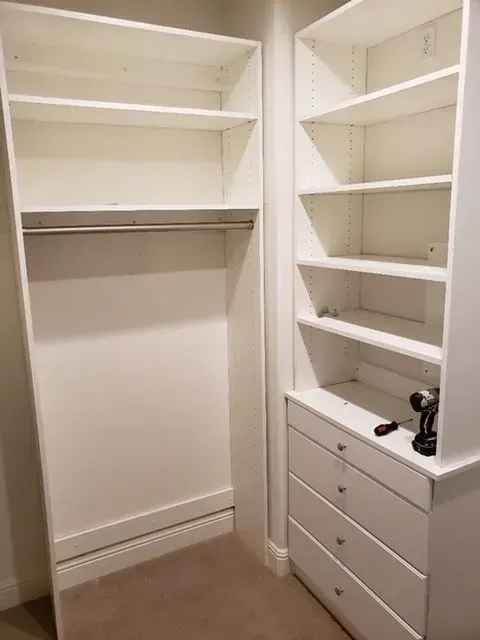 White built-in closet with shelves, drawers, and a hanging rod, empty and under construction, set in a room with beige carpet.