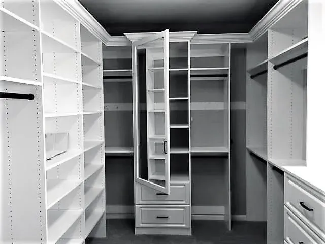 Walk-in closet with white shelves, drawers, and hanging rods. Center has a pivoting mirrored cabinet.