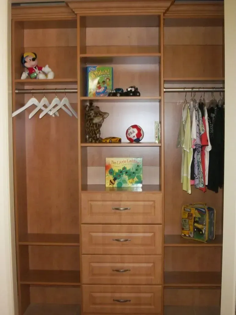 Wooden closet organizer with shelves, drawers, and hanging rods; some clothing and toys are visible.