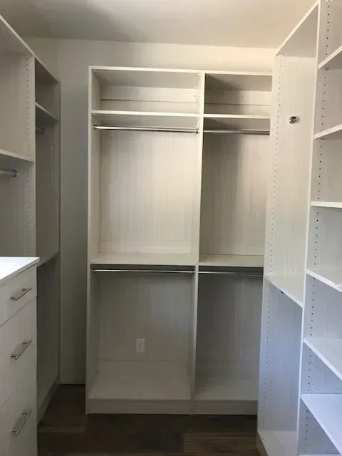 White walk-in closet with shelves and rods for hanging clothes; light brown floor.