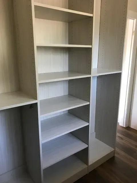 White built-in closet shelving unit with multiple shelves and a low base, against a neutral wall.