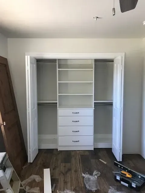 White closet organizer installed inside a closet with bi-fold doors, hardwood floor.