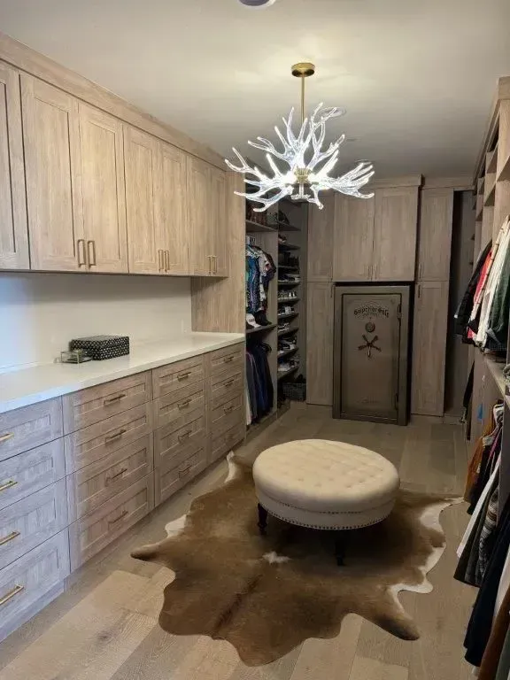 Walk-in closet with light wood cabinets, drawers, and a tan cowhide rug. Antler chandelier and round ottoman.