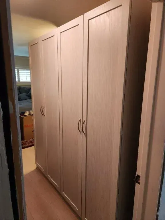 Four beige wardrobe doors in a hallway. The doors have simple handles and vertical wood grain.