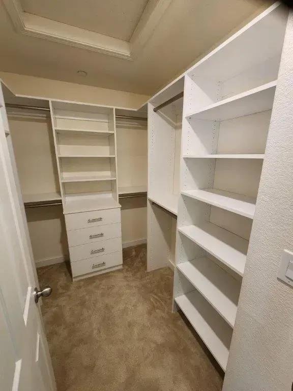 White custom closet with shelving, drawers, and hanging rods. Carpeted floor.