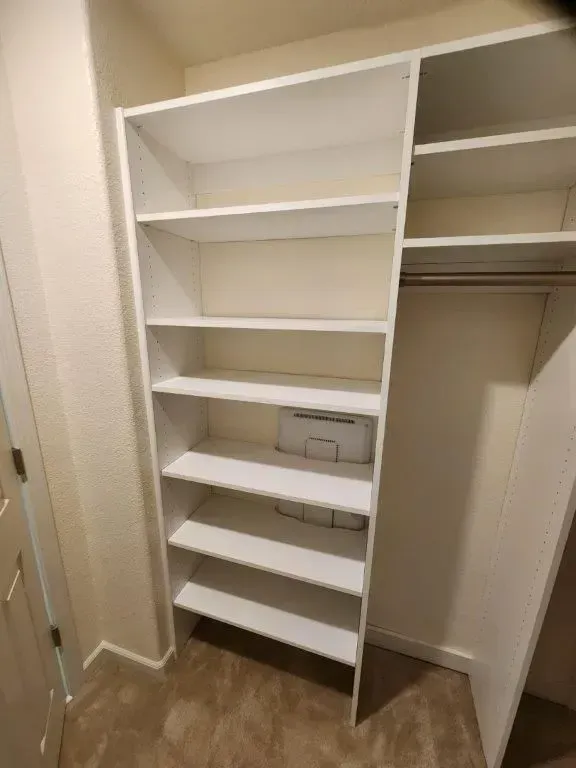 White closet shelving unit with multiple shelves, adjacent to a hanging rod.