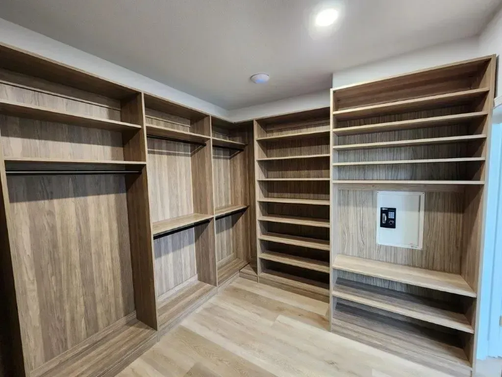 Empty walk-in closet with built-in wooden shelves and hanging rods; light-colored wood flooring.