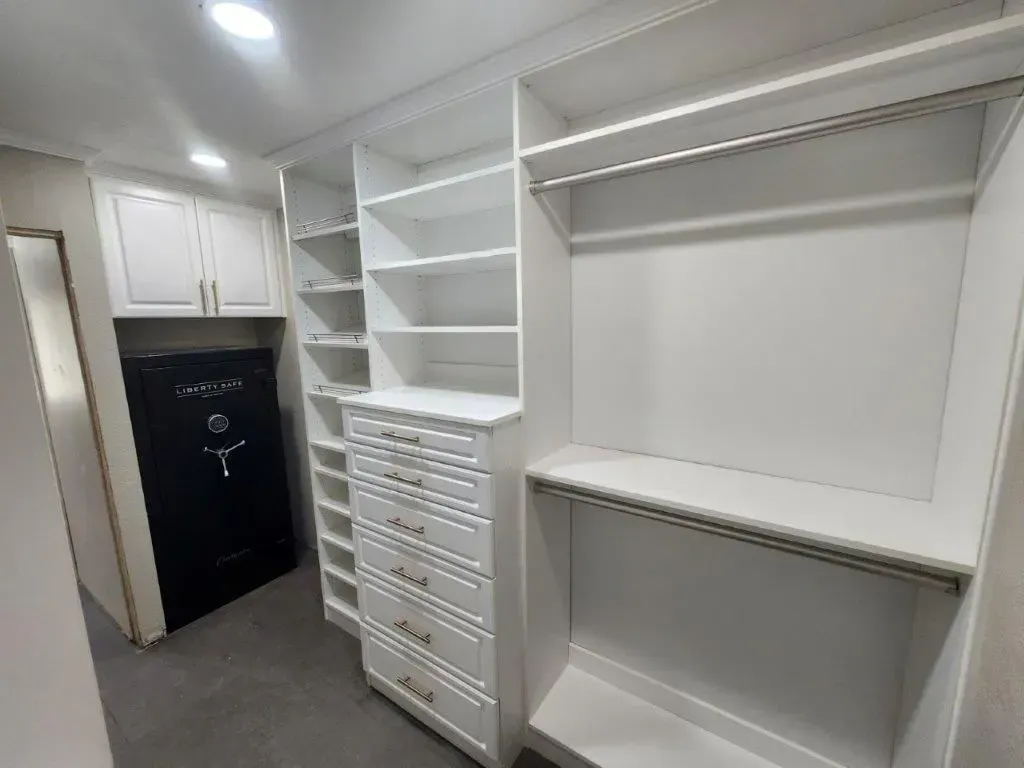 White custom closet system with shelves, drawers, and hanging rods. Includes a black safe.