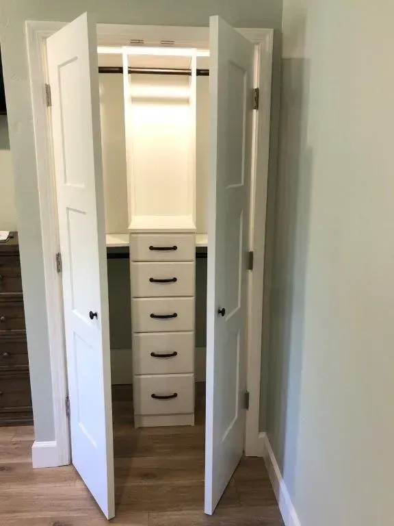 White closet with bi-fold doors open, revealing drawers and hanging space.