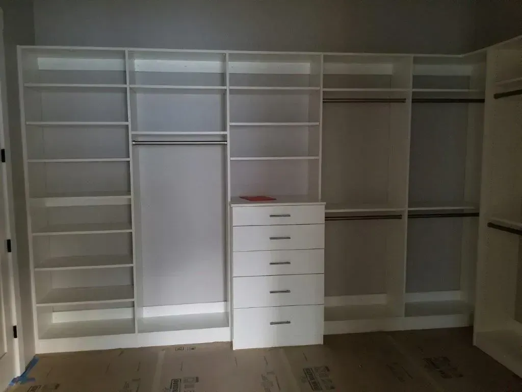 White walk-in closet with shelves, hanging rods, and a dresser.