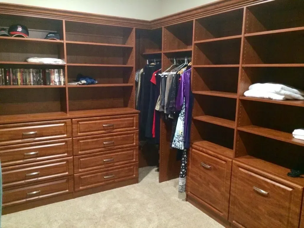 Walk-in closet with wooden shelves, drawers, and hanging rods filled with clothes.