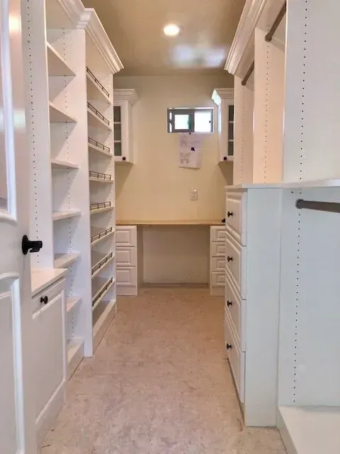 White closet with shelves, drawers, and a built-in desk. Beige walls and flooring.