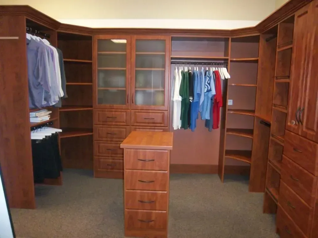 Walk-in closet with dark wood cabinetry, including hanging rods, shelves, and a central dresser.