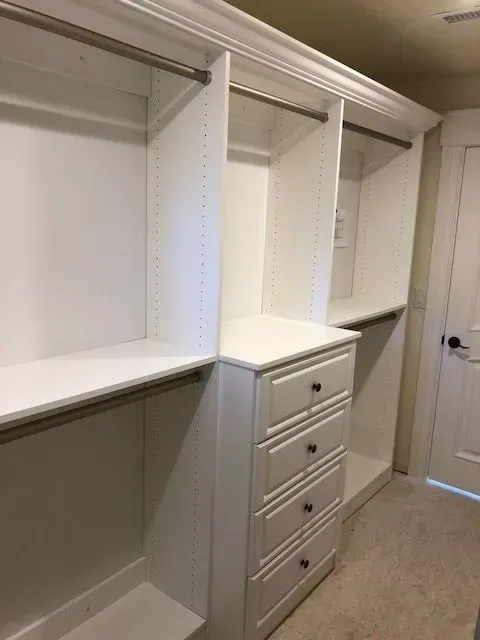 White built-in closet with shelves, drawers, and hanging rods. The door is on the right side.