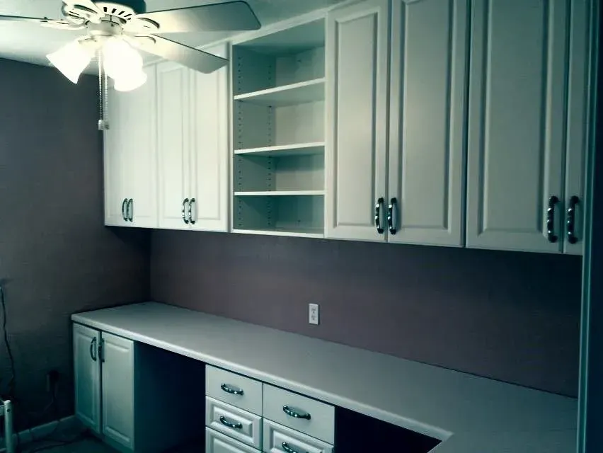 White cabinets and desk with open shelves. Purple wall. Ceiling fan.