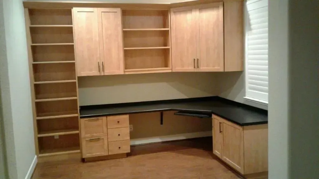 Built-in home office with light wood cabinets, dark countertop, and open shelving.