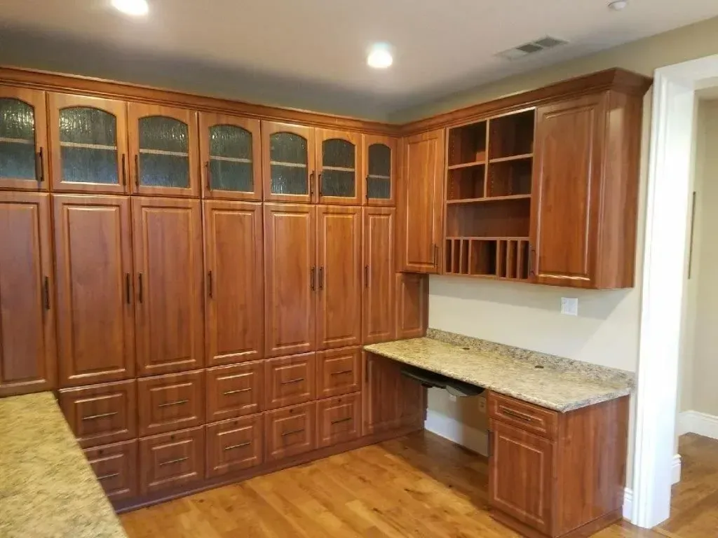 Wooden built-in cabinets with glass-fronted upper sections, a desk with granite countertop, and wood flooring.
