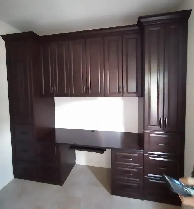 Dark brown built-in desk with cabinets and drawers, in a room with white walls.