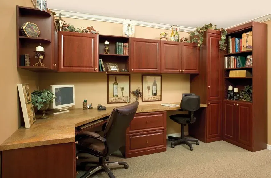 Home office with cherry-colored cabinets, corner desk, and two office chairs. Beige walls and carpet.