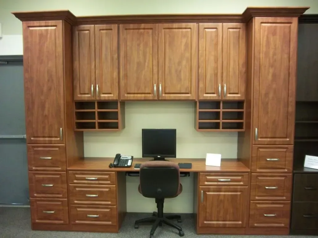 Wooden office desk setup with cabinets and hutch. Includes a computer, phone, and chair.