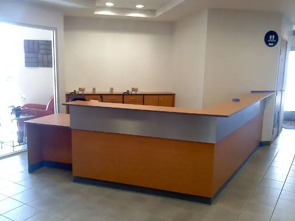 Orange and silver reception desk in an office setting, with a white wall and side entrance.