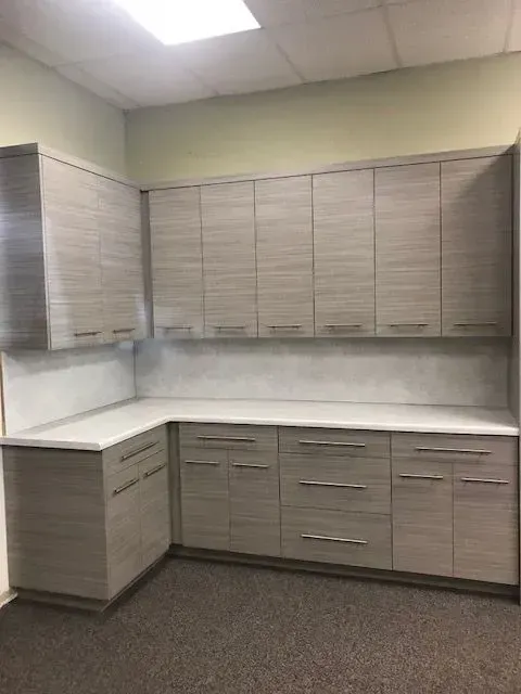 L-shaped cabinets with light wood-grain doors and white countertops in a room with a brown carpet.