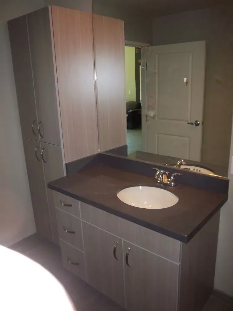 Bathroom vanity with tall cabinet, dark countertop, and open door to hallway.