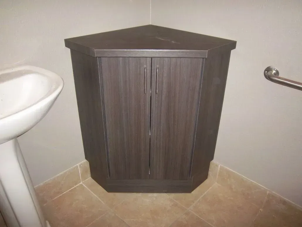 Dark corner cabinet with two doors, next to a white sink and a grab bar in a tiled bathroom.