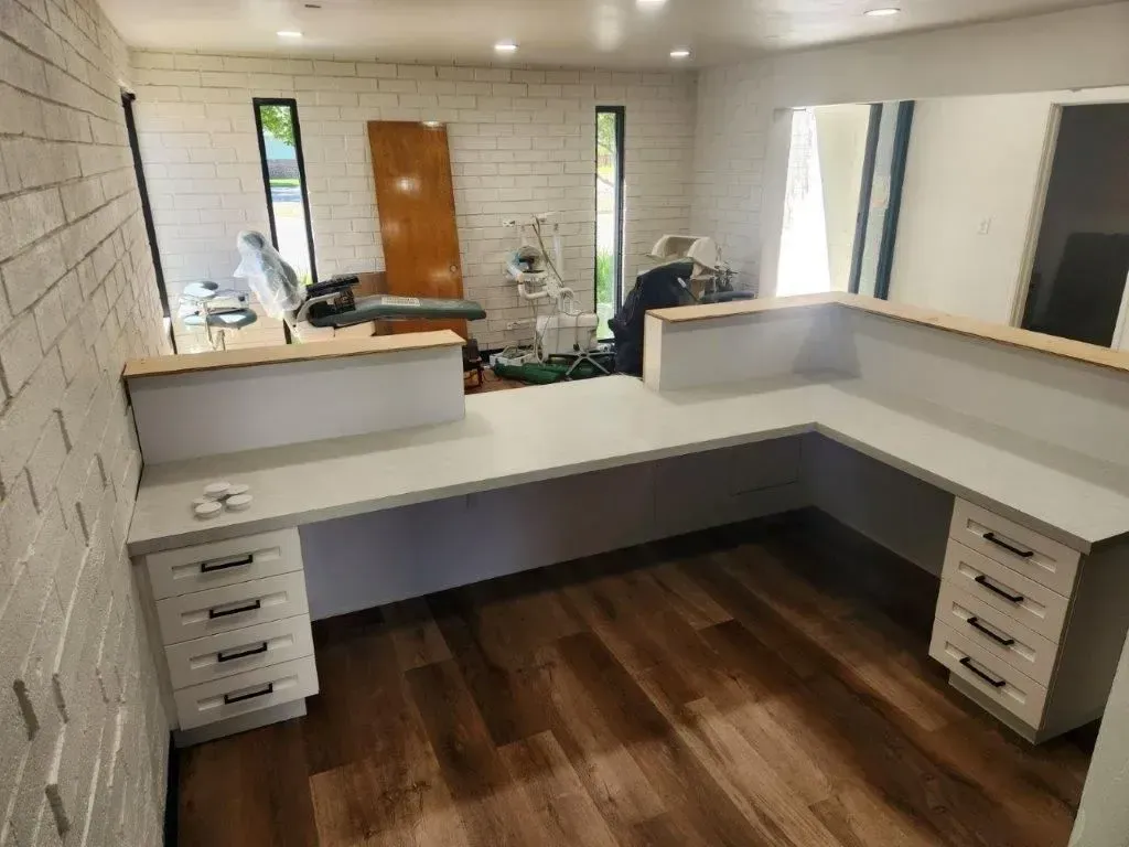 L-shaped reception desk in a room with wood floors and white brick wall.
