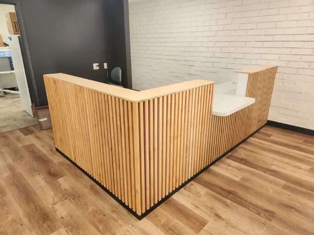 Wooden slat reception desk in a modern office space with white brick wall.