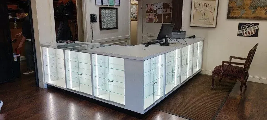 Corner display case in a store, with bright lighting and glass panels. An antique chair sits nearby.