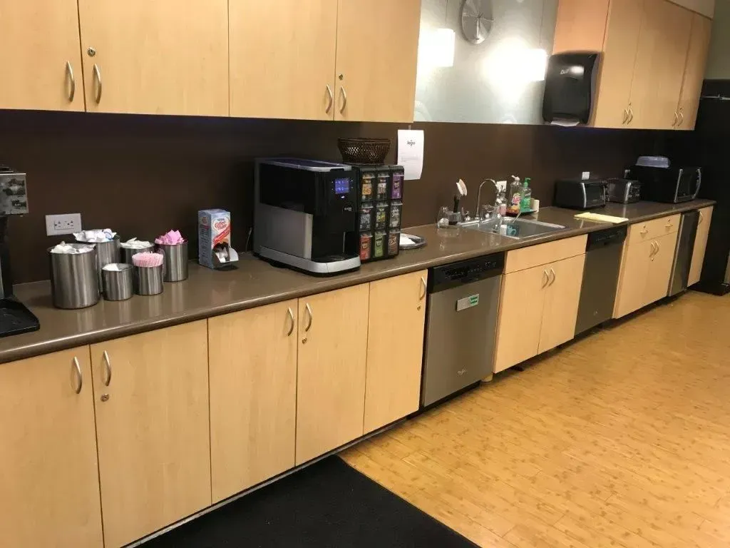 Office break room with counters, cabinets, sink, coffee machine, and appliances.