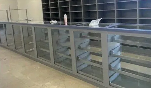 Long gray retail counter with glass panels and shelves, in front of a gray shelving unit.